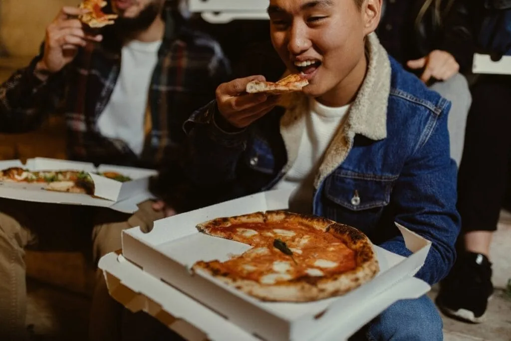 Asian male eating pizza with friends late night